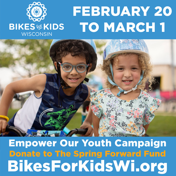 Photo of two young kids smiling and posing with their helmets and bikes