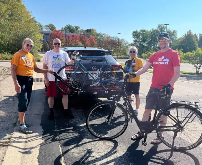 four people posing next to the back of a car with bikes for donation