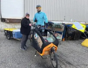 Two people standing by a cargo bike with trailer loaded with groceries