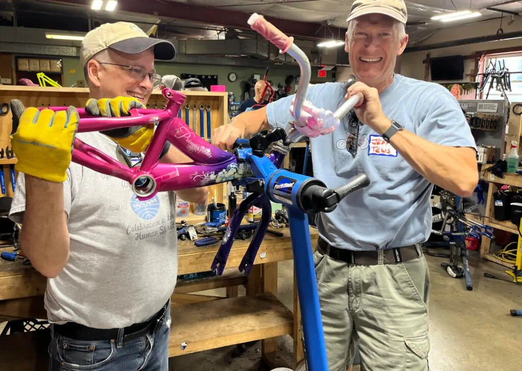 Two men working on a bike and smiling at Bikes for Kids